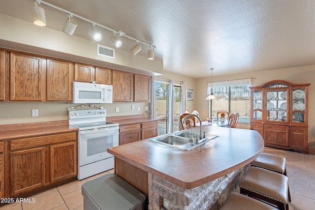 kitchen with sink, a breakfast bar area, pendant lighting, white appliances, and a kitchen island with sink