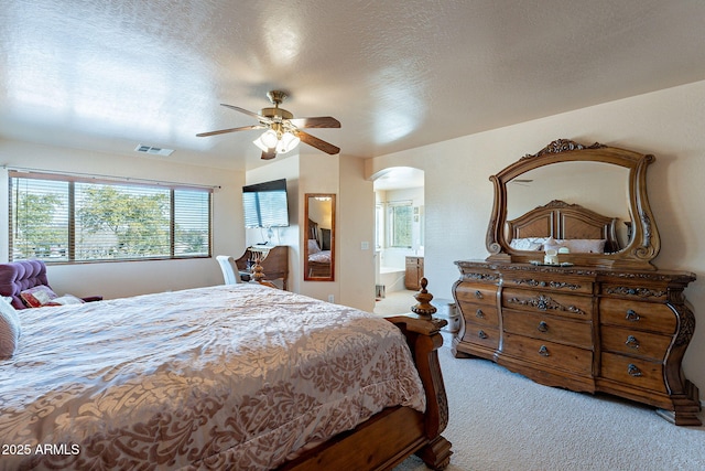 carpeted bedroom with ceiling fan, ensuite bathroom, and a textured ceiling