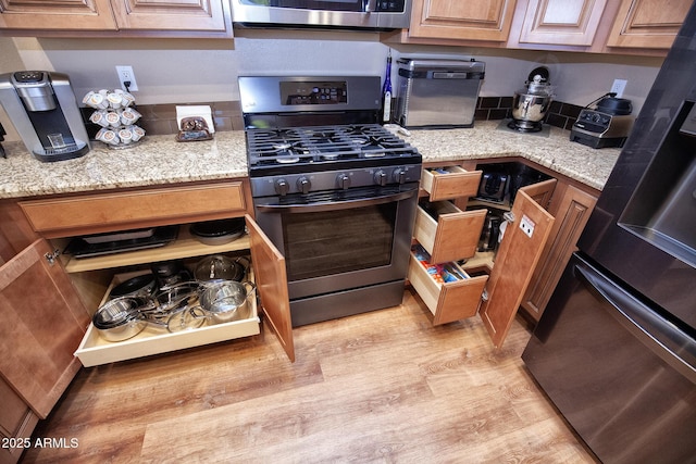 kitchen featuring appliances with stainless steel finishes, light wood-type flooring, and light stone countertops