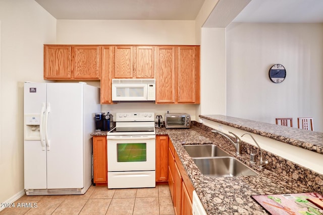 kitchen featuring dark stone countertops, sink, white appliances, and light tile patterned floors