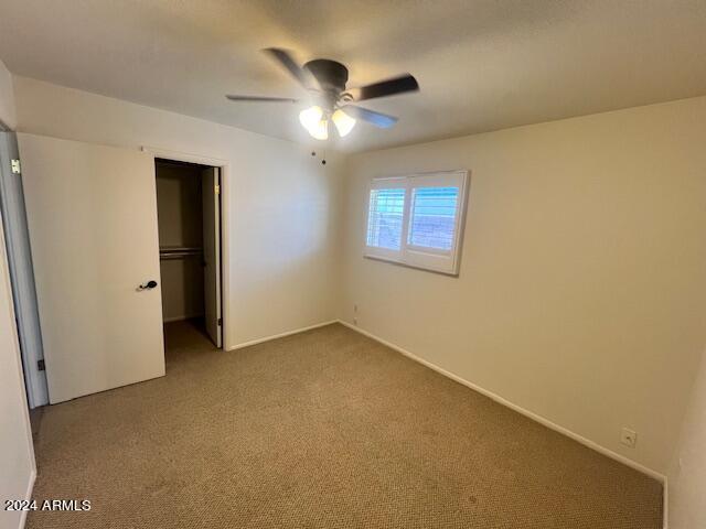 unfurnished bedroom with a walk in closet, carpet floors, a closet, and ceiling fan