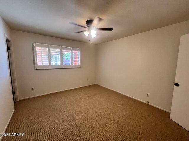 empty room featuring ceiling fan and dark carpet