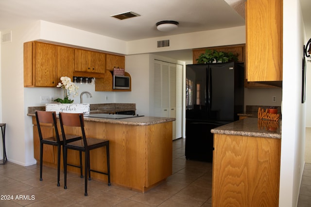 kitchen with stainless steel microwave, black refrigerator, dark tile patterned floors, a kitchen bar, and kitchen peninsula