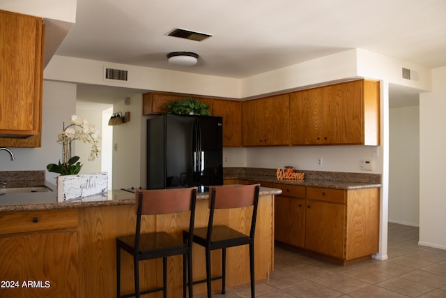 kitchen featuring sink, black fridge, kitchen peninsula, a kitchen bar, and light tile patterned floors