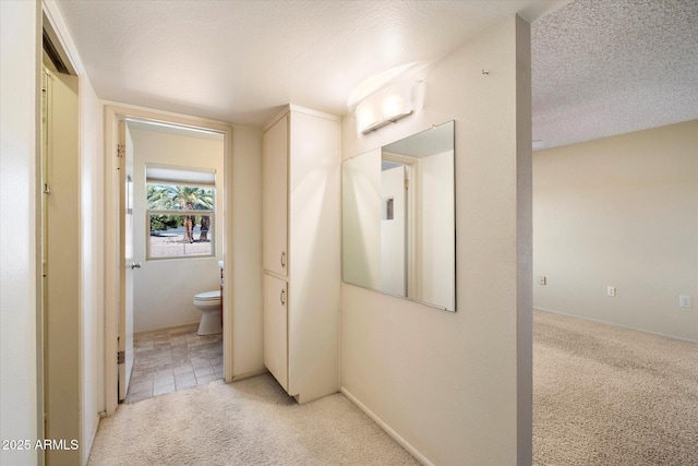 hall with a textured ceiling, light tile patterned floors, and light colored carpet