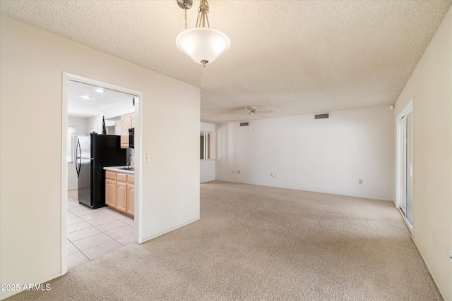 empty room featuring light tile patterned floors, visible vents, light colored carpet, a ceiling fan, and a textured ceiling