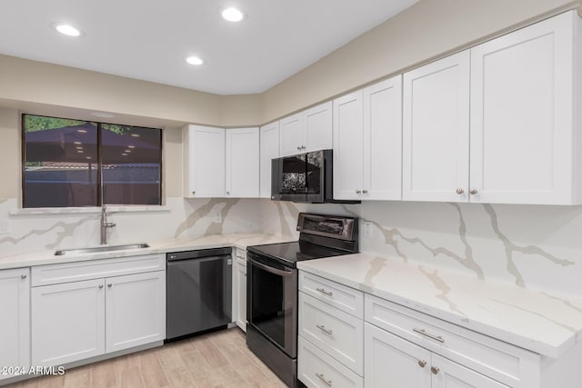 kitchen with stainless steel electric stove, black dishwasher, sink, white cabinets, and light stone counters