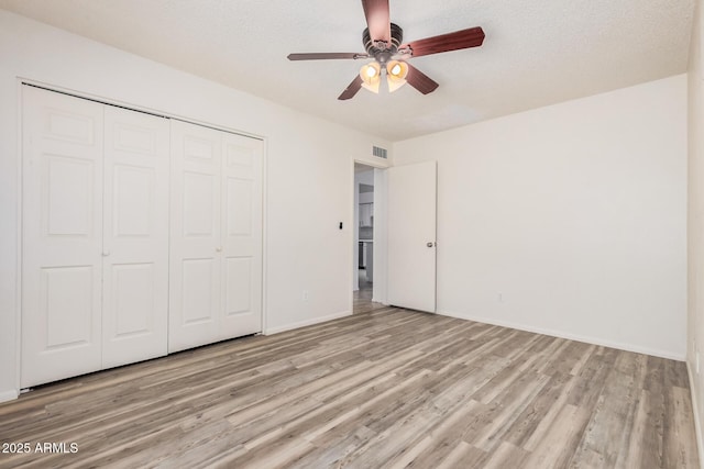 unfurnished bedroom featuring a closet, ceiling fan, light wood-style flooring, baseboards, and visible vents
