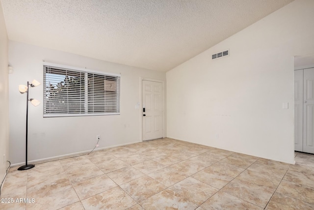 empty room featuring lofted ceiling, a textured ceiling, visible vents, and light tile patterned floors
