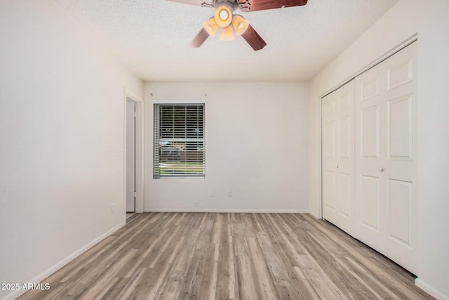 unfurnished bedroom with baseboards, light wood-style floors, a textured ceiling, and a closet