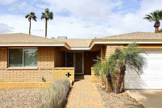 doorway to property with concrete driveway, an attached garage, brick siding, and roof with shingles