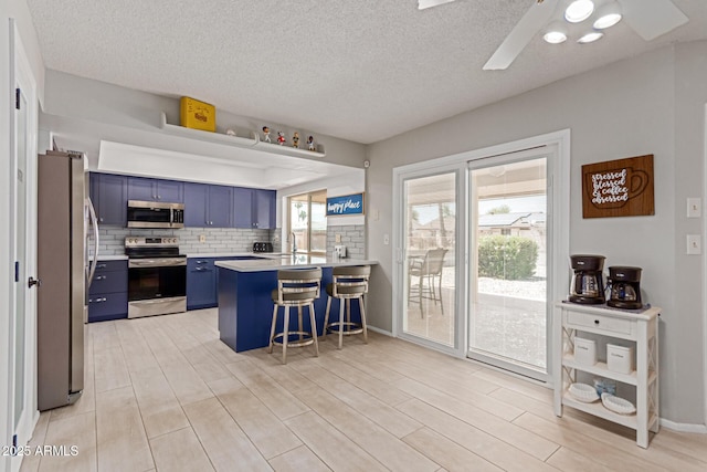 kitchen featuring a breakfast bar, a wealth of natural light, kitchen peninsula, stainless steel appliances, and blue cabinetry