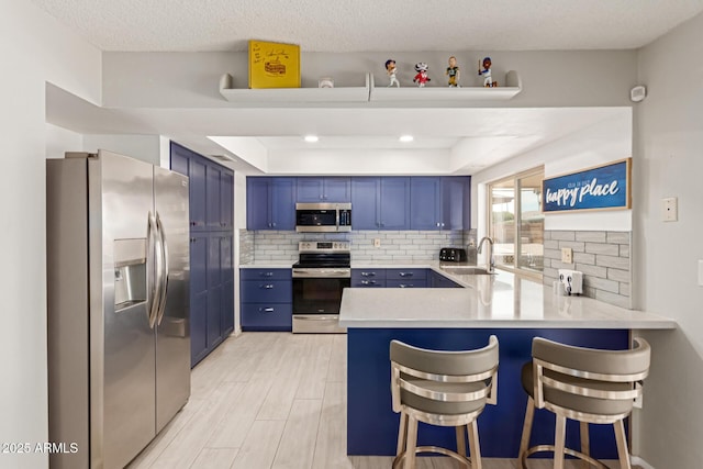 kitchen with blue cabinets, a breakfast bar area, kitchen peninsula, stainless steel appliances, and backsplash