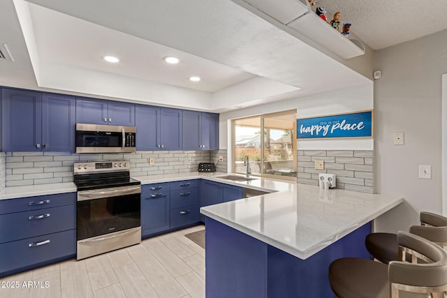 kitchen featuring sink, a breakfast bar, appliances with stainless steel finishes, blue cabinets, and kitchen peninsula