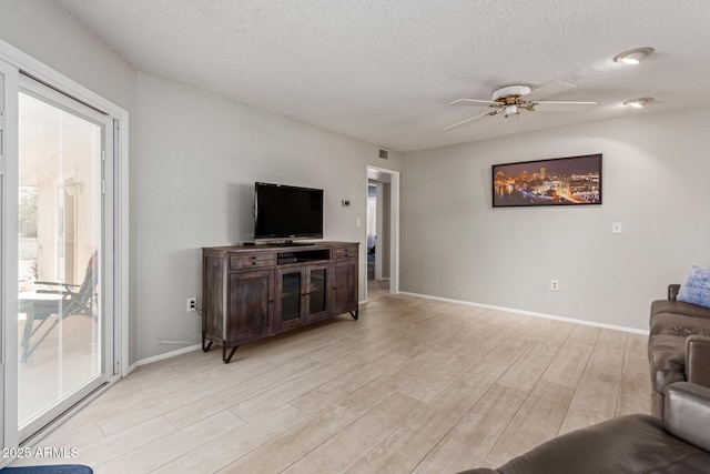 living room featuring ceiling fan, light hardwood / wood-style floors, and a textured ceiling