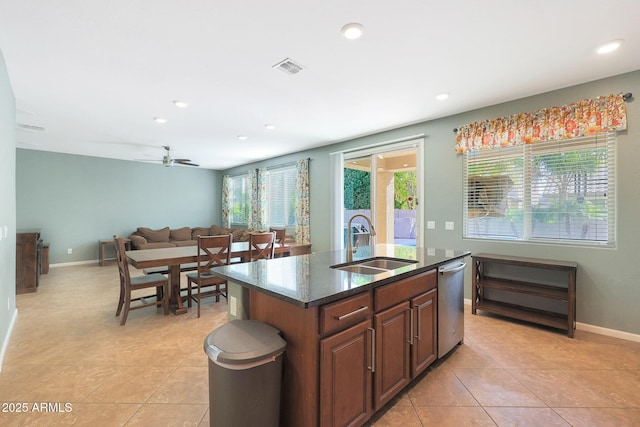 kitchen featuring dishwasher, an island with sink, sink, dark stone counters, and a healthy amount of sunlight