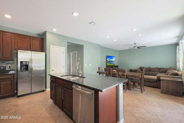 kitchen with sink, light tile patterned floors, appliances with stainless steel finishes, backsplash, and a center island with sink