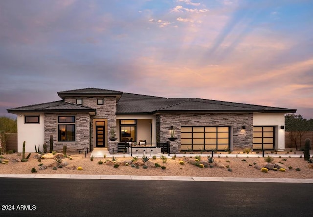 prairie-style house with stone siding, an attached garage, and stucco siding