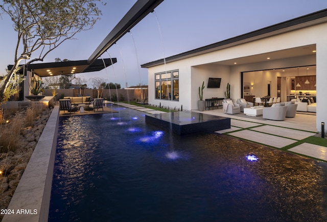 pool at dusk featuring pool water feature, an outdoor living space, and a patio