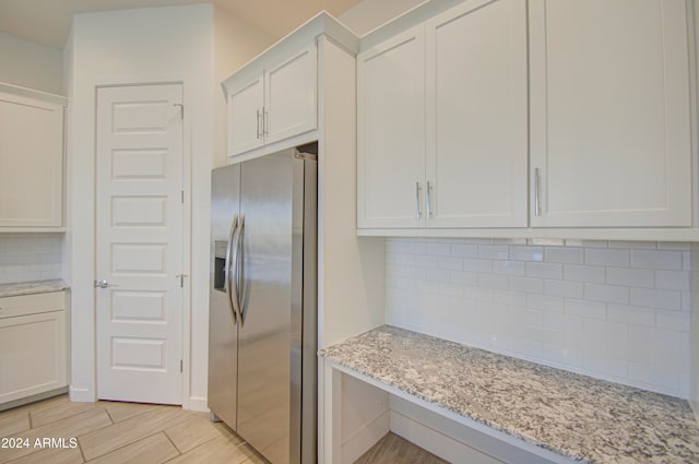 kitchen with backsplash, white cabinets, stainless steel refrigerator with ice dispenser, light hardwood / wood-style flooring, and light stone counters