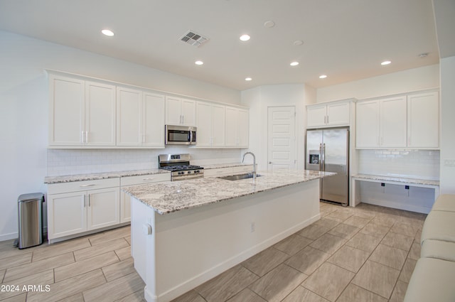 kitchen with light stone countertops, stainless steel appliances, sink, a center island with sink, and white cabinetry