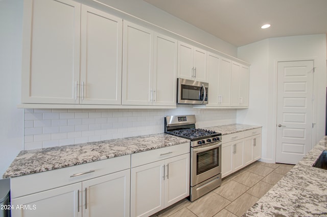 kitchen featuring backsplash, light stone countertops, white cabinetry, and stainless steel appliances