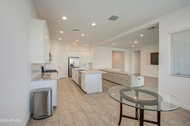 kitchen featuring appliances with stainless steel finishes, backsplash, a kitchen island with sink, sink, and white cabinetry