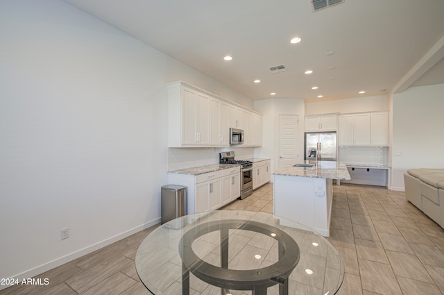 kitchen featuring light stone countertops, sink, stainless steel appliances, a center island with sink, and white cabinets