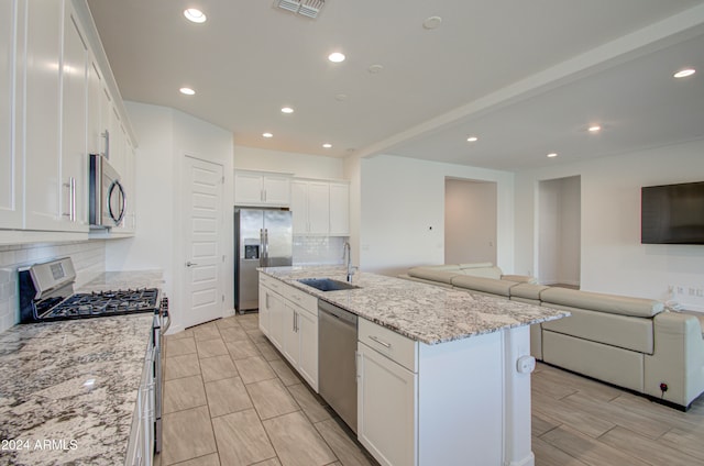 kitchen with tasteful backsplash, stainless steel appliances, sink, white cabinetry, and an island with sink