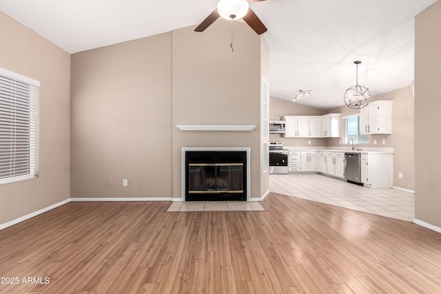 unfurnished living room with a sink, a fireplace with flush hearth, lofted ceiling, and light wood finished floors