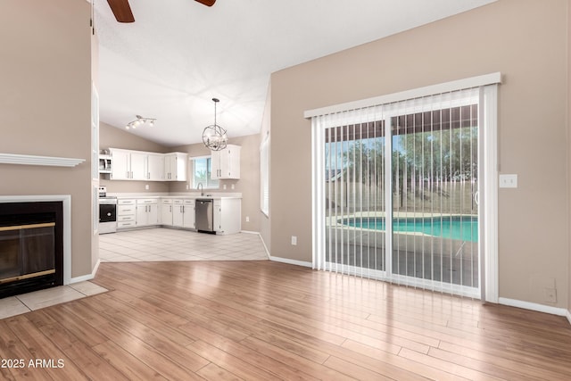 unfurnished living room with vaulted ceiling, light wood-style flooring, a fireplace with flush hearth, and a sink