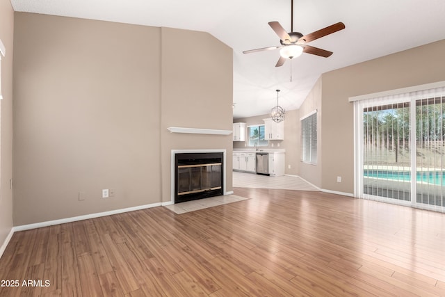 unfurnished living room with baseboards, light wood finished floors, lofted ceiling, a fireplace with flush hearth, and ceiling fan with notable chandelier