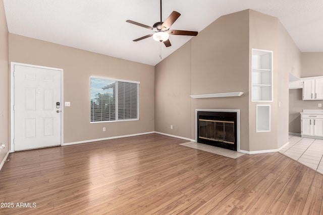 unfurnished living room featuring built in shelves, a fireplace with flush hearth, lofted ceiling, light wood-style flooring, and a ceiling fan