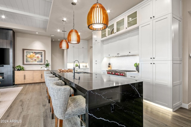 kitchen with dark stone counters, white cabinets, an island with sink, light hardwood / wood-style floors, and stainless steel gas stovetop