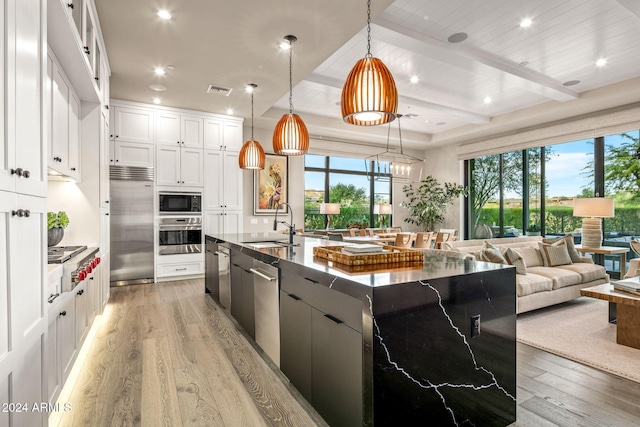 kitchen featuring built in appliances, hanging light fixtures, a spacious island, white cabinets, and light wood-type flooring