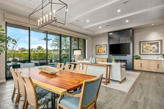 dining room featuring a chandelier, wood-type flooring, a large fireplace, and beam ceiling