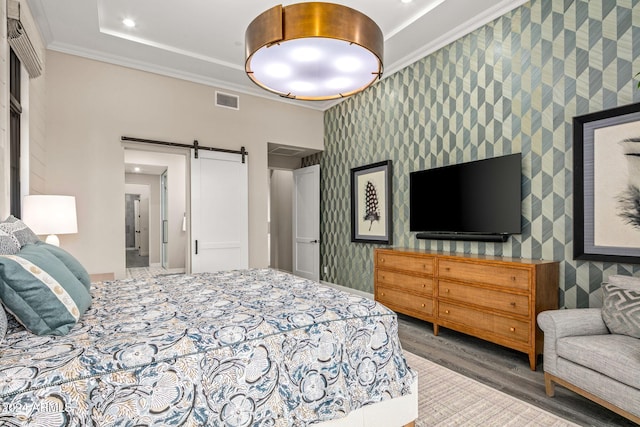 bedroom featuring a barn door, ornamental molding, and hardwood / wood-style floors