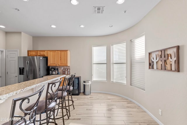 kitchen featuring backsplash, stainless steel fridge with ice dispenser, light hardwood / wood-style floors, and a kitchen breakfast bar