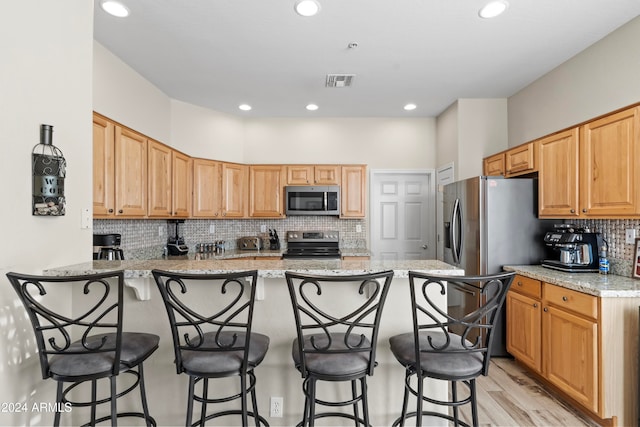 kitchen with kitchen peninsula, appliances with stainless steel finishes, light stone counters, and a breakfast bar area