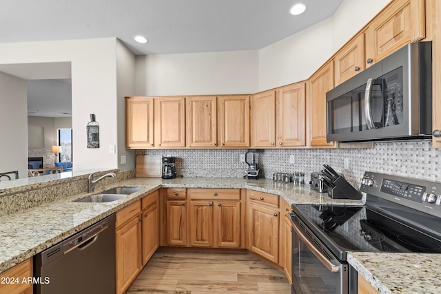 kitchen featuring tasteful backsplash, appliances with stainless steel finishes, light stone countertops, sink, and light hardwood / wood-style floors