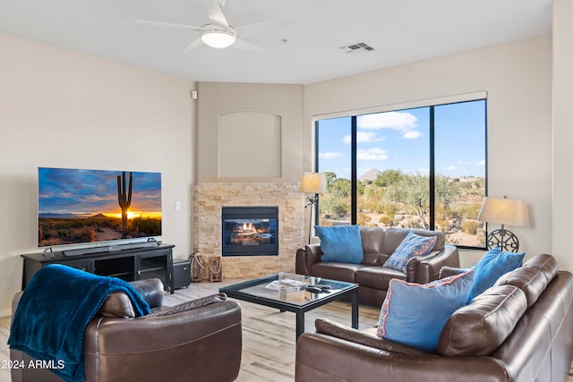 living room featuring a stone fireplace, light wood-type flooring, and ceiling fan