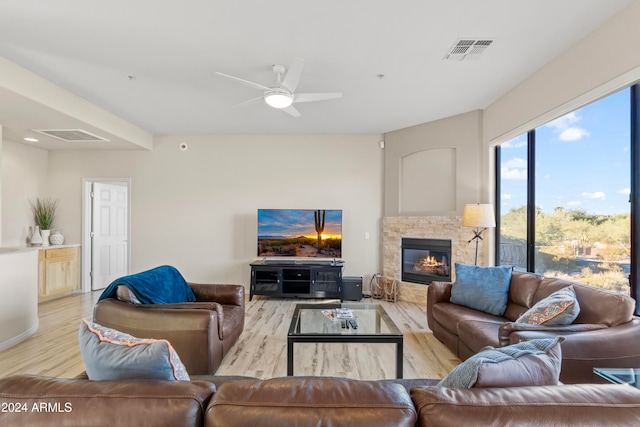 living room featuring a stone fireplace, light hardwood / wood-style floors, and ceiling fan