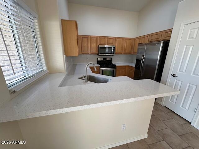 20275 N 81st Ln, Peoria, AZ 85382 - kitchen featuring stainless steel appliances, a sink, a peninsula, brown cabinetry, and tile patterned floors