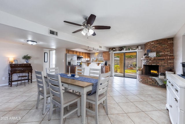 tiled dining space with ceiling fan and a fireplace