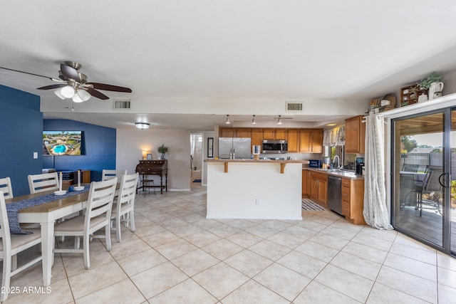 kitchen featuring light tile patterned flooring, a kitchen bar, sink, a center island, and appliances with stainless steel finishes