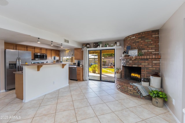 kitchen with appliances with stainless steel finishes, light tile patterned floors, a kitchen breakfast bar, and a brick fireplace