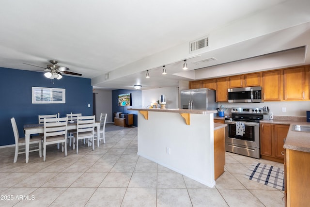 kitchen featuring light tile patterned floors, ceiling fan, appliances with stainless steel finishes, a kitchen island, and a kitchen bar