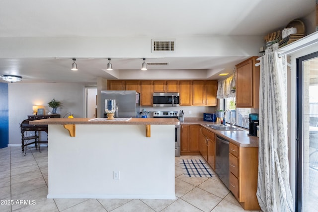 kitchen featuring light tile patterned flooring, appliances with stainless steel finishes, sink, a kitchen bar, and a center island