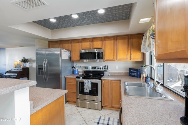 kitchen featuring light tile patterned flooring, appliances with stainless steel finishes, sink, and a tray ceiling