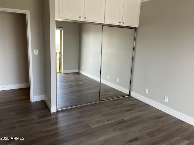 unfurnished bedroom with baseboards, a closet, and dark wood-type flooring